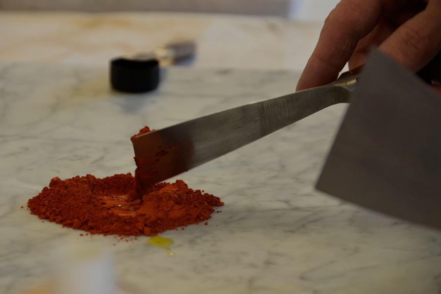 Handwerkliche Herstellung einer Ölfarbe: Auf einer Marmorplatte wird das rote Ockerpigment mit Öl gemischt.