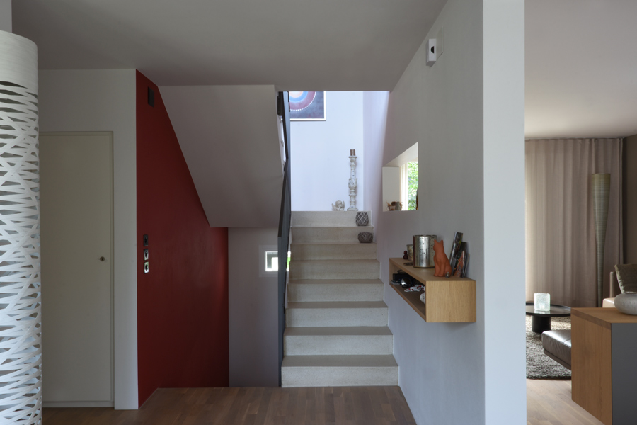  Farbgestaltung Innenraum: Das Bild zeigt den Wohnraum mit Treppenhaus mir einer Wand in Rot und die andere in abgetöntem Weiss.