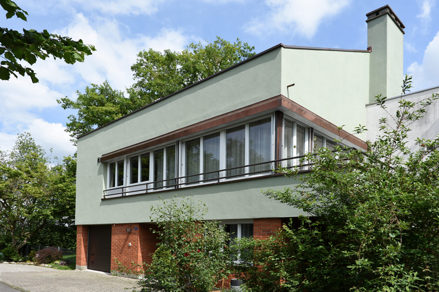  Farbgestaltung Fassade: Das Bild zeigt die neu renovierte Fassade eines Einfamilienhauses aus den 50er Jahren mit dezent grünem Putz, der mit dem Backstein im Eingangsgeschoss harmoniert.