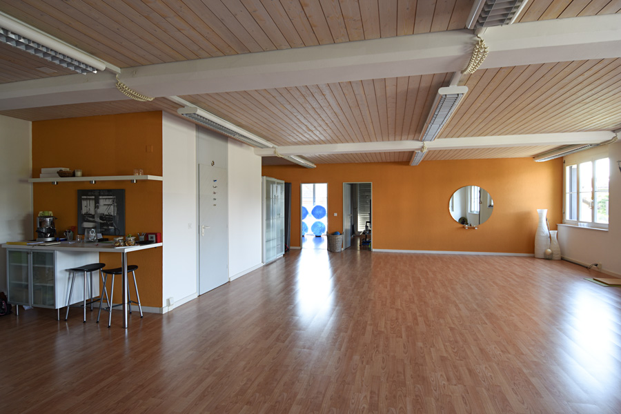 Farbkonzept + Gesundheitsraum: Das Bild zeigt die Farbgestaltung für den Gruppenraum in einem Yoga und Pilates Studio - Erdiges Ockerorange harmoniert mit Weiss, Grau und heller Holzdecke.