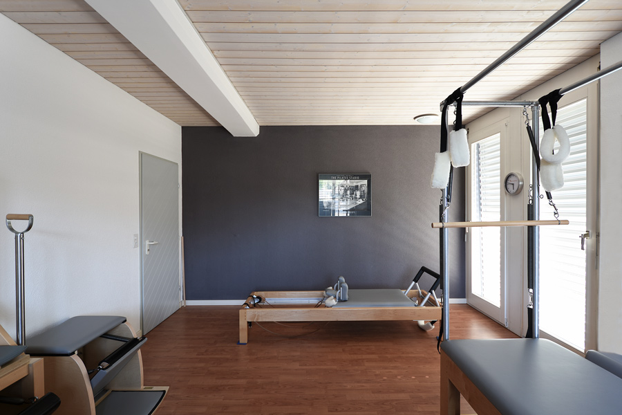 Farbkonzept + Gesundheitsraum: Das Bild zeigt die Farbgestaltung für die Wände des Raums für Personal Training in einem Yoga und Pilates Studio - Die Farbgebung von Violett-Anthrazit, warmes Weiss und heller Holzdecke harmoniert mit den Geräten