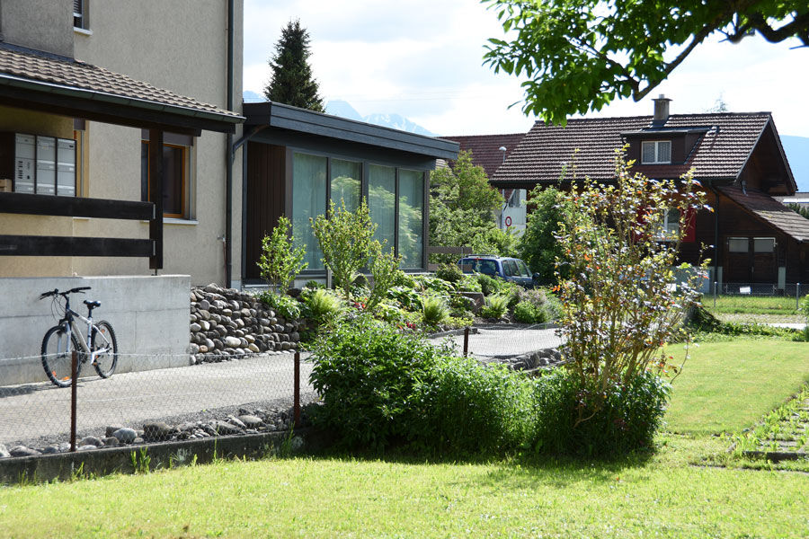 Farbgestaltung Holzfassade: Das Bild zeigt von der Strasse aus die Eingangsseite des Atelieranbaus mit der grossen Fensterfront auf der Nordseite.